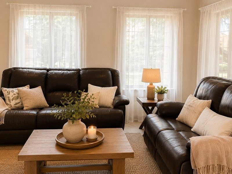 A bright and comfortable living room featuring neutral walls, tiled flooring, and large windows that allow for ample natural light.