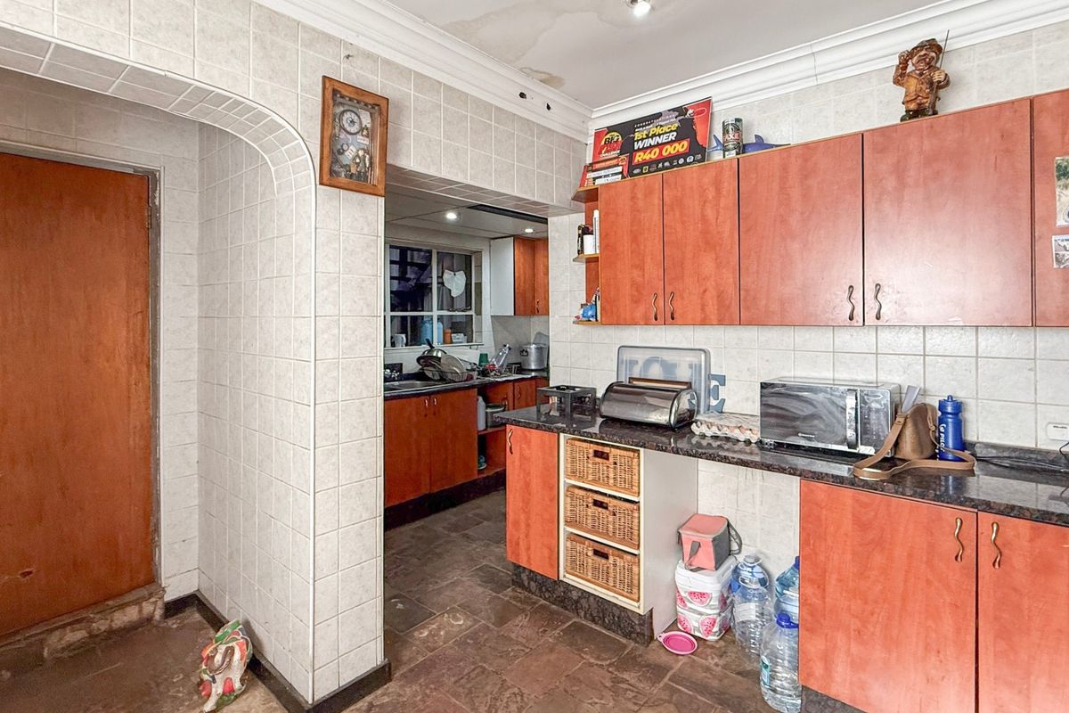 A dated kitchen featuring laminate cabinetry, granite countertops, and tiled finishes, with visible ceiling water damage requiring attention.