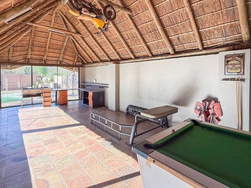 Spacious covered patio featuring a traditional thatched roof, exposed timber rafters, tiled flooring, and large sliding glass doors overlooking the pool area.