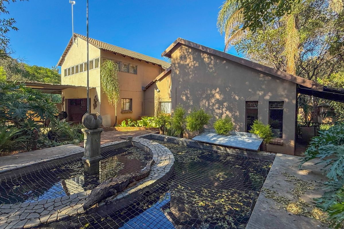 Rear view of the property featuring a large pond with a central fountain, paved patio area, and established garden surroundings.