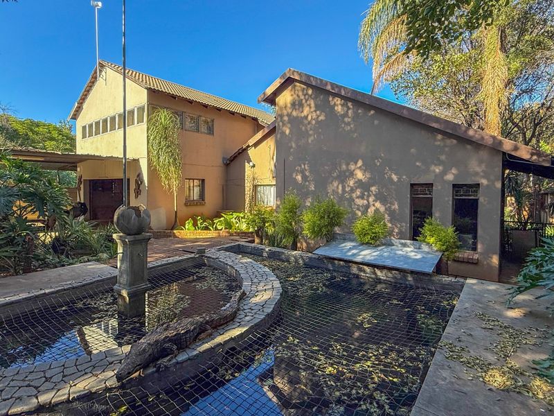 Rear view of the property featuring a large pond with a central fountain, paved patio area, and established garden surroundings.