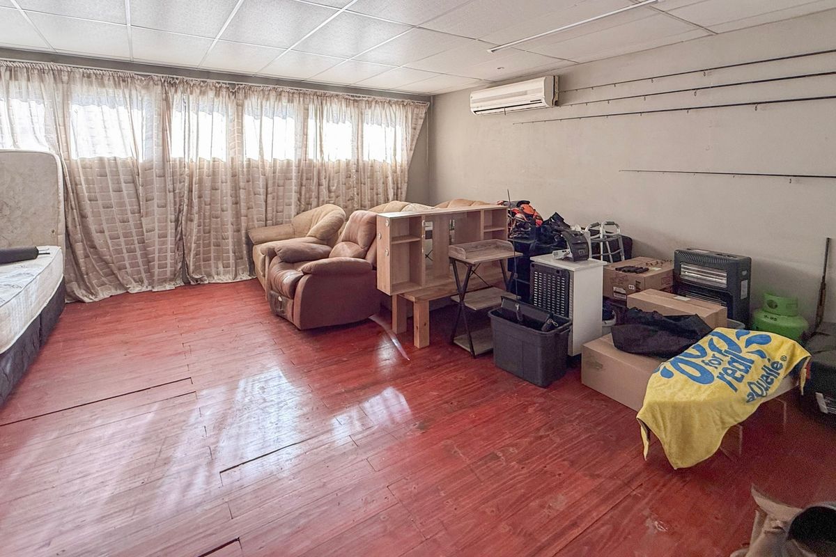 Spacious living area featuring timber flooring, a split-system air conditioner, and a suspended ceiling, offering potential for renovation and modernization.