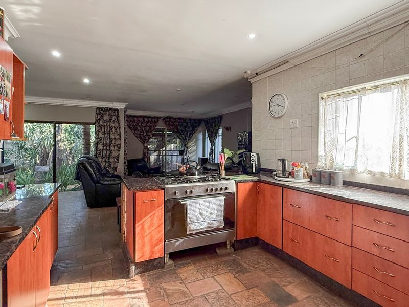 Open-plan kitchen featuring wooden cabinetry, stone countertops, and a gas stove, seamlessly flowing into the adjacent living area with tiled flooring throughout.