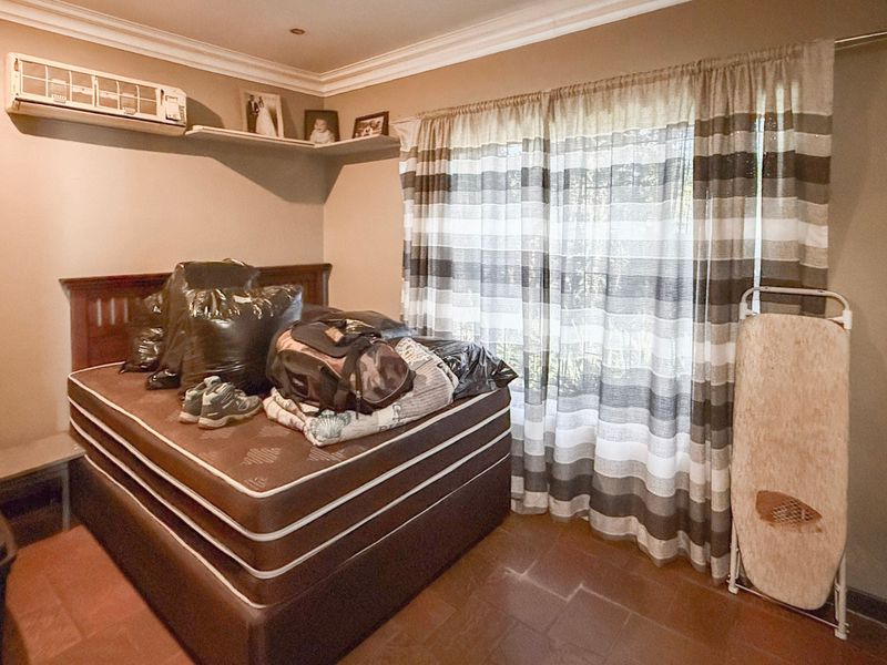 A bedroom featuring tiled flooring, coving, and a wall-mounted air conditioning unit, offering a functional space with natural light.
