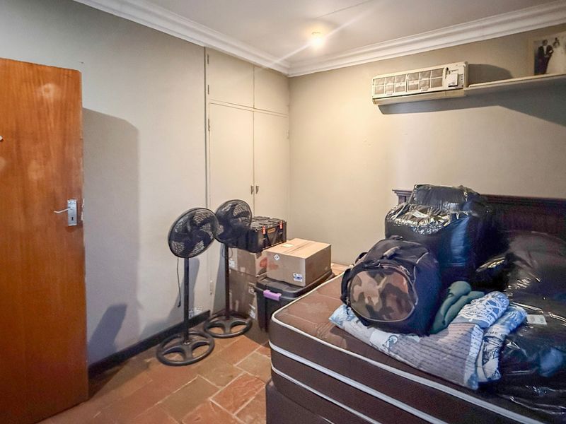 A bedroom featuring built-in cupboards, tiled flooring, and a wall-mounted air conditioning unit.