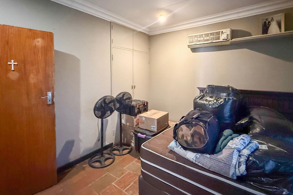 A bedroom featuring built-in cupboards, tiled flooring, and a wall-mounted air conditioning unit.