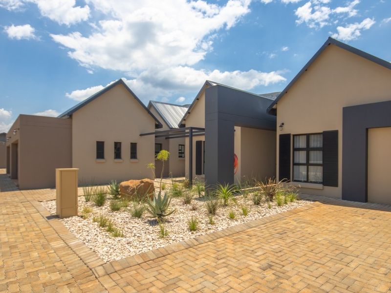 Modern townhouse exterior featuring a paved driveway, landscaped garden bed, and contemporary architectural design with neutral tones and dark accents.