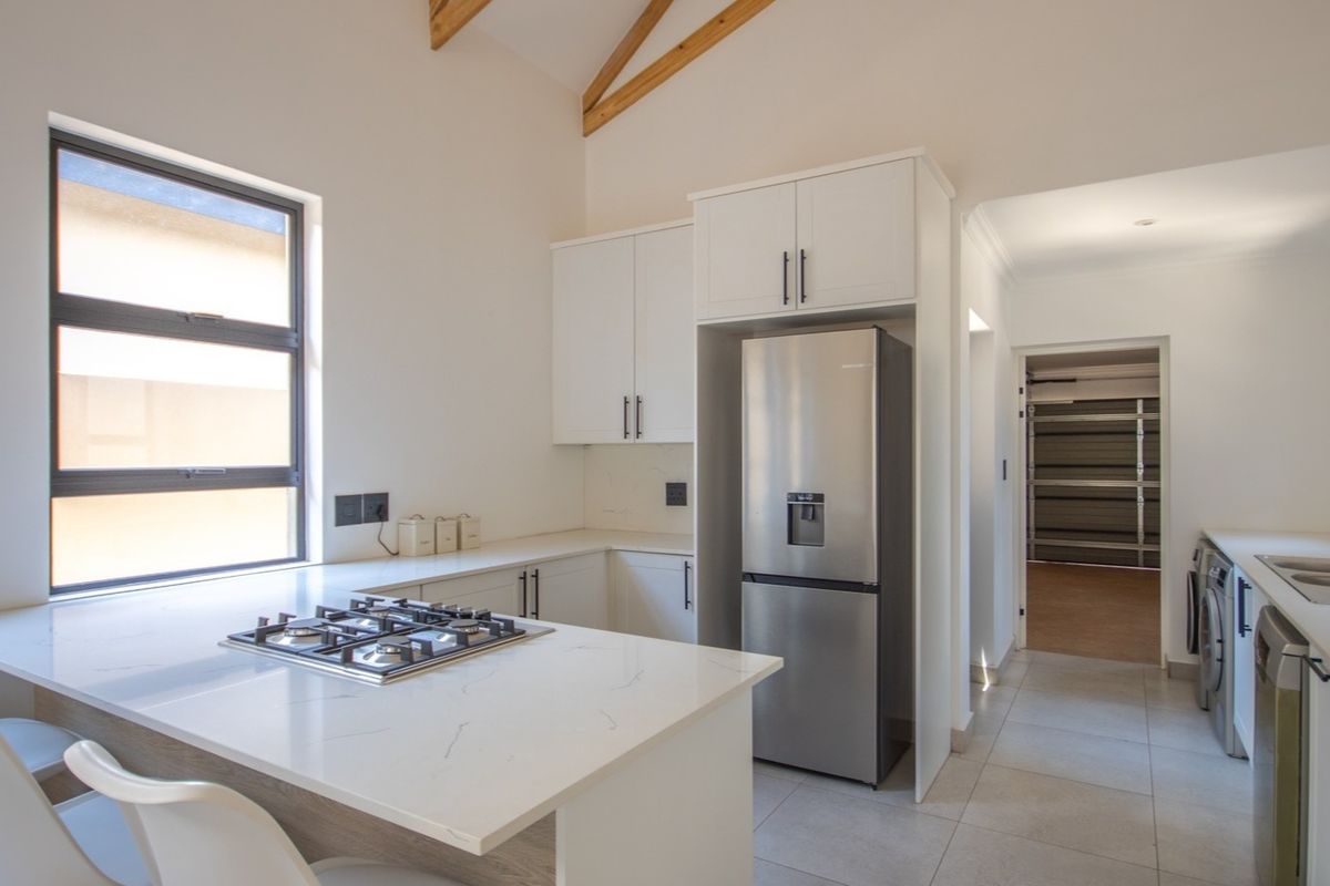 Modern kitchen featuring quartz countertops, a gas hob, built-in cabinetry, and exposed timber rafters, with an adjacent laundry area and direct garage access.