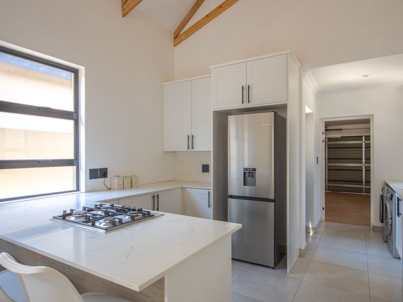 Modern kitchen featuring quartz countertops, a gas hob, built-in cabinetry, and exposed timber rafters, with an adjacent laundry area and direct garage access.