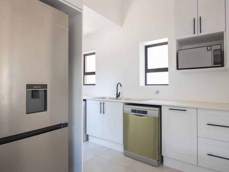 Modern kitchen featuring white cabinetry, sleek black hardware, integrated microwave, stainless steel sink, and tiled flooring in a clean, minimalist layout.