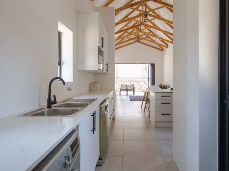 Modern open-plan kitchen and living area featuring high vaulted ceilings with exposed timber trusses, sleek cabinetry, quartz countertops, and seamless access to the patio.