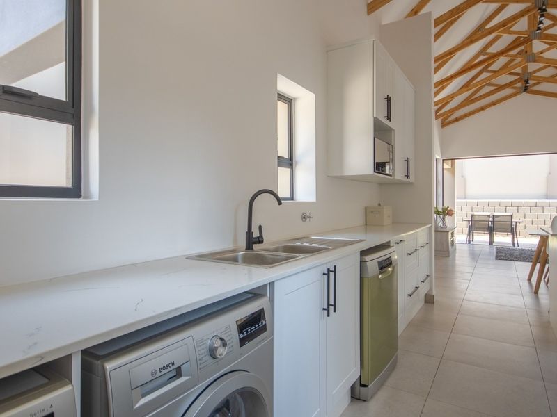 Modern scullery featuring quartz countertops, double sink, sleek cabinetry, and exposed timber roof trusses, leading out to a patio area.