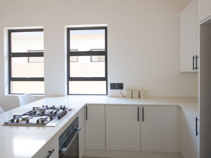 Modern kitchen featuring white shaker-style cabinetry, quartz countertops, a built-in gas hob, and an oven, complemented by large aluminium-framed windows.