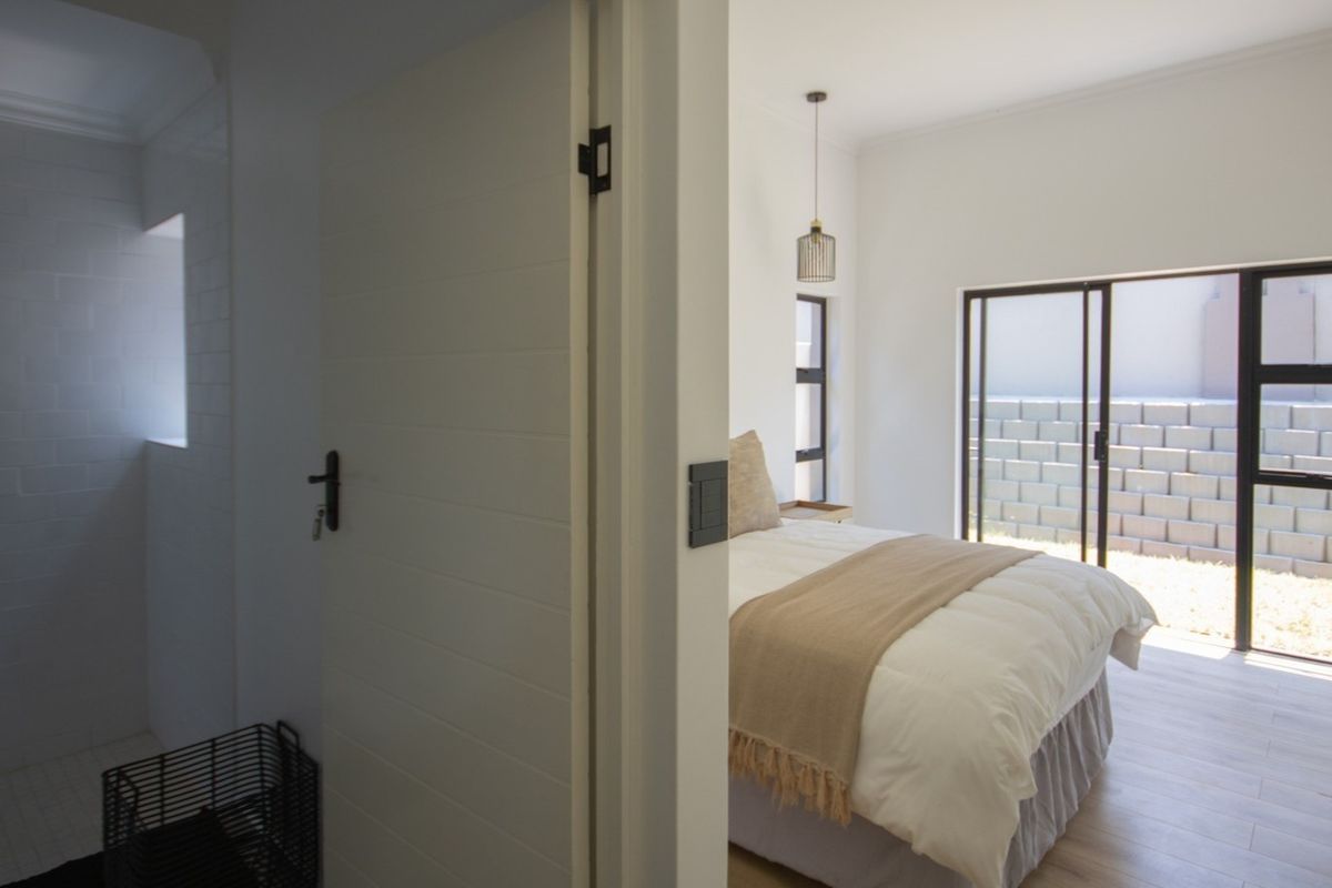 A bright bedroom featuring modern sliding glass doors leading to an outdoor area, adjacent to a clean, tiled bathroom space.