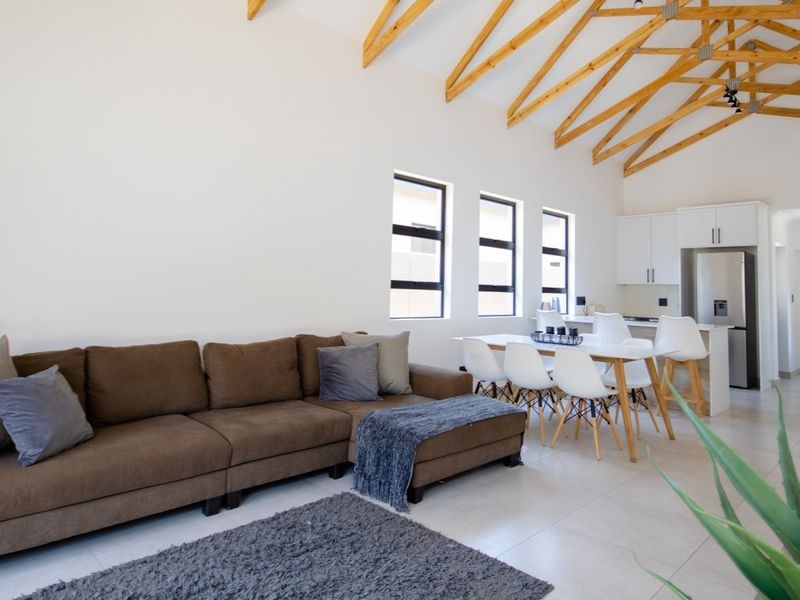 Spacious open-plan living and dining area featuring high vaulted ceilings with exposed timber trusses, tiled floors, and a modern kitchen with built-in cabinetry.