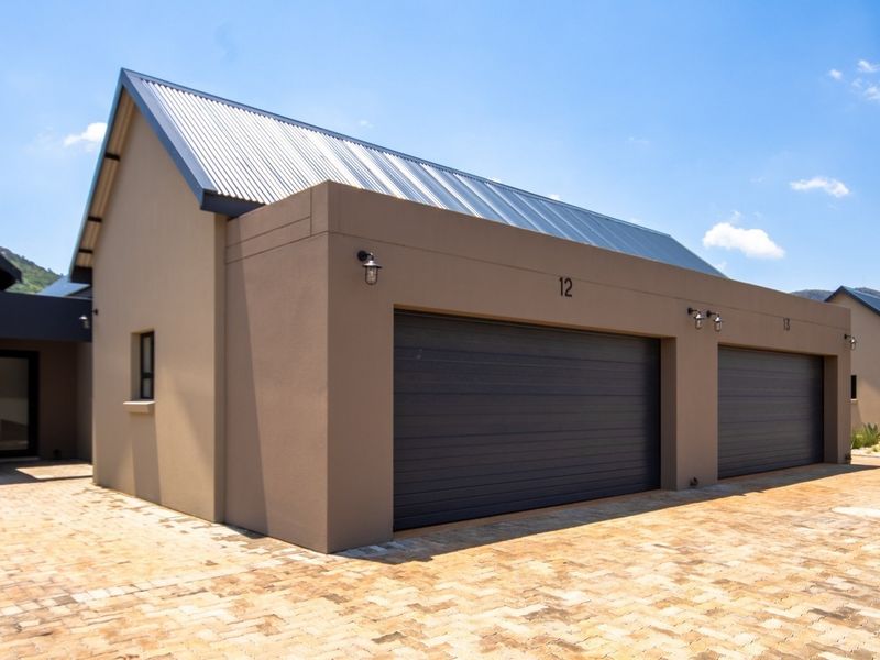 A modern townhouse exterior featuring a double garage with dark sectional doors, a corrugated metal roof, and a neatly paved driveway.