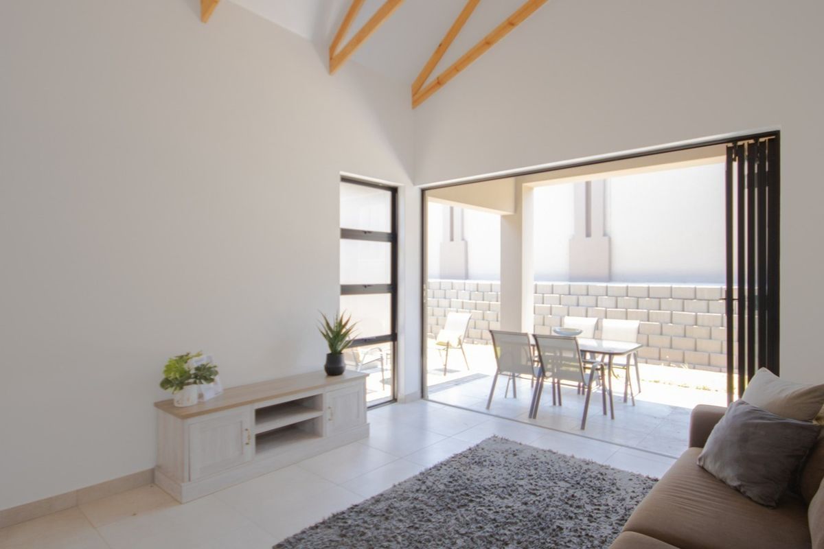 Bright living room featuring a high vaulted ceiling with exposed timber rafters, tiled floors, and large stacking doors opening onto a patio.