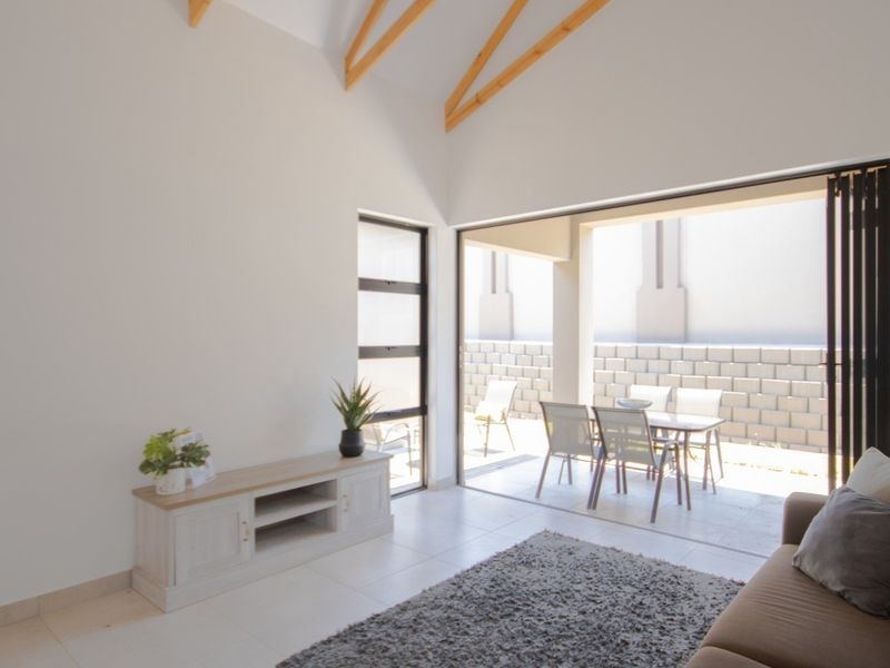 Bright living room featuring a high vaulted ceiling with exposed timber rafters, tiled floors, and large stacking doors opening onto a patio.