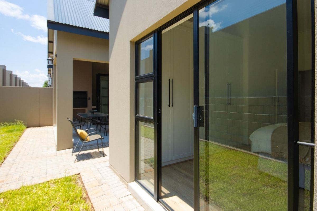Rear view of the townhouse featuring a paved patio area with a built-in braai and sliding glass doors leading into the bedroom.