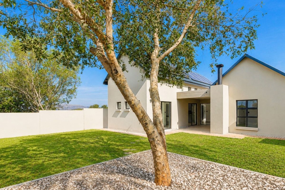 Rear view of the townhouse featuring a private garden, covered patio area, boundary wall, and solar panels installed on the roof.