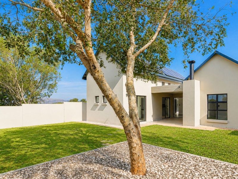 Rear view of the townhouse featuring a private garden, covered patio area, boundary wall, and solar panels installed on the roof.