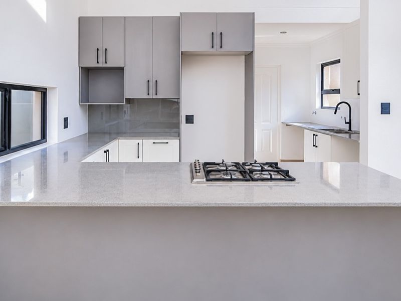 Modern kitchen featuring sleek grey and white cabinetry, quartz countertops, a built-in gas hob, and a separate scullery area with a sink.