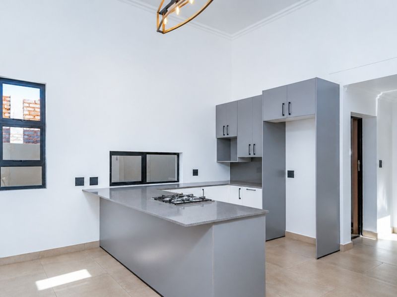 Modern kitchen featuring sleek grey cabinetry, stone countertops, a built-in gas hob, and tiled flooring in a bright, open-plan layout.