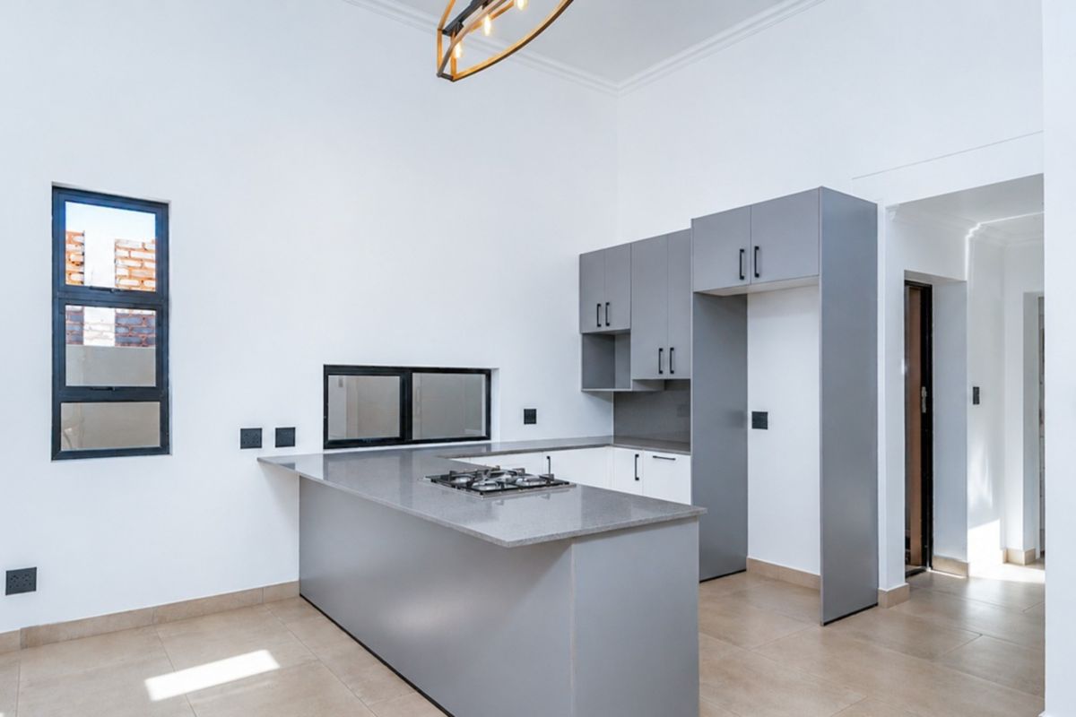 Modern kitchen featuring sleek grey cabinetry, stone countertops, a built-in gas hob, and tiled flooring in a bright, open-plan layout.