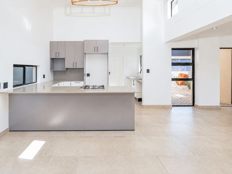 Spacious open-plan kitchen and living area featuring modern cabinetry, stone countertops, gas hob, and large tiled flooring with direct access to the outdoor area.