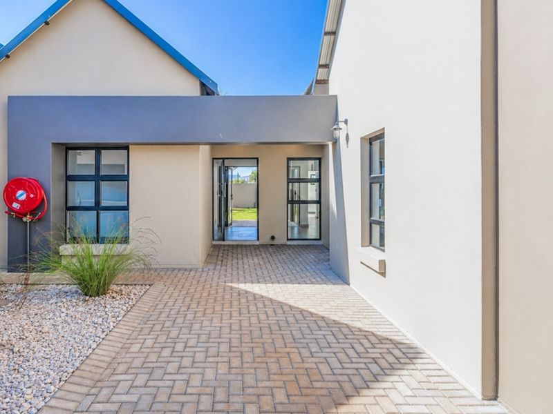 A modern townhouse entrance featuring a paved walkway, clean rendered walls, and contemporary aluminium-framed windows and doors.