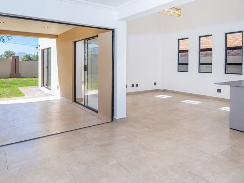 Spacious open-plan living area featuring modern tiled flooring, a sleek kitchen island with built-in appliances, and seamless access to the outdoor patio through bi-fold doors.
