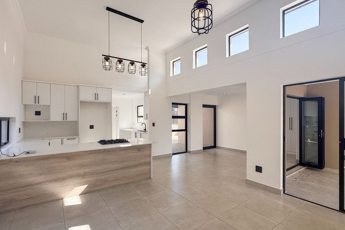 Modern open-plan living and kitchen area featuring a central island, gas hob, sleek cabinetry, tiled floors, and abundant natural light from high-level windows.