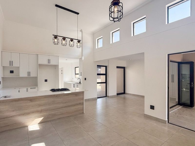 Modern open-plan living and kitchen area featuring a central island, gas hob, sleek cabinetry, tiled floors, and abundant natural light from high-level windows.