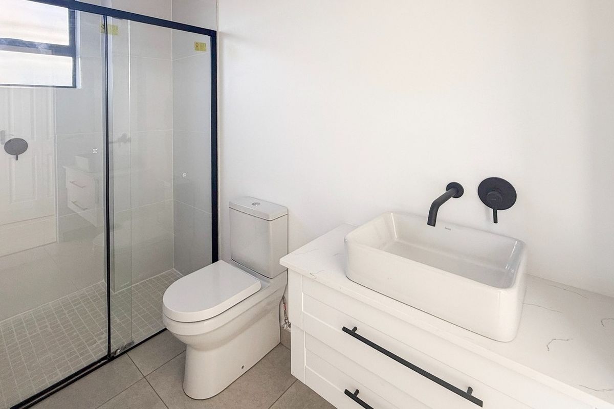 Modern bathroom featuring a glass-enclosed shower with black fixtures, a contemporary vessel sink on a vanity cabinet, and clean white finishes.