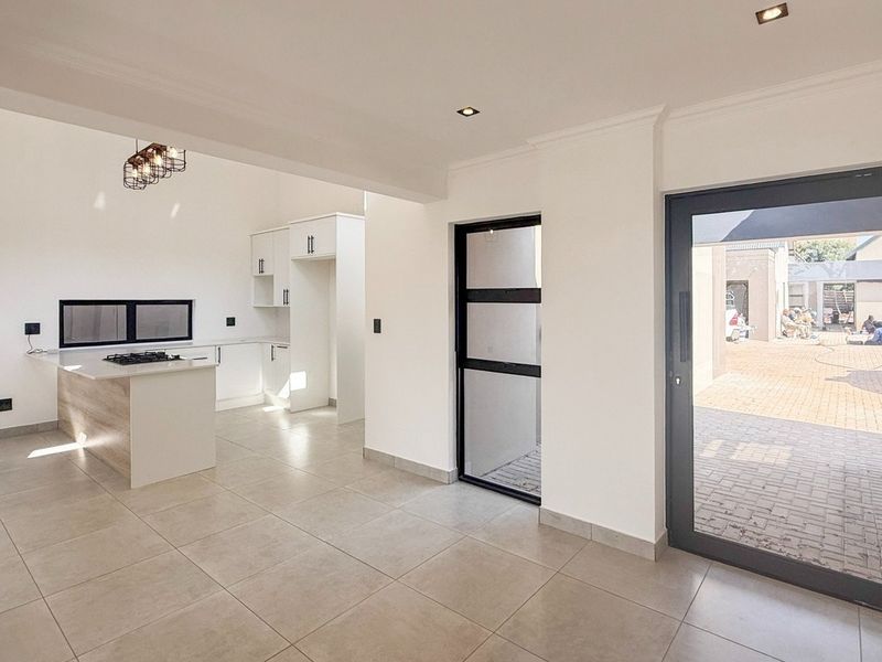 Modern open-plan kitchen and living area featuring tiled floors, sleek cabinetry, a central island with a gas hob, and direct access to the patio.