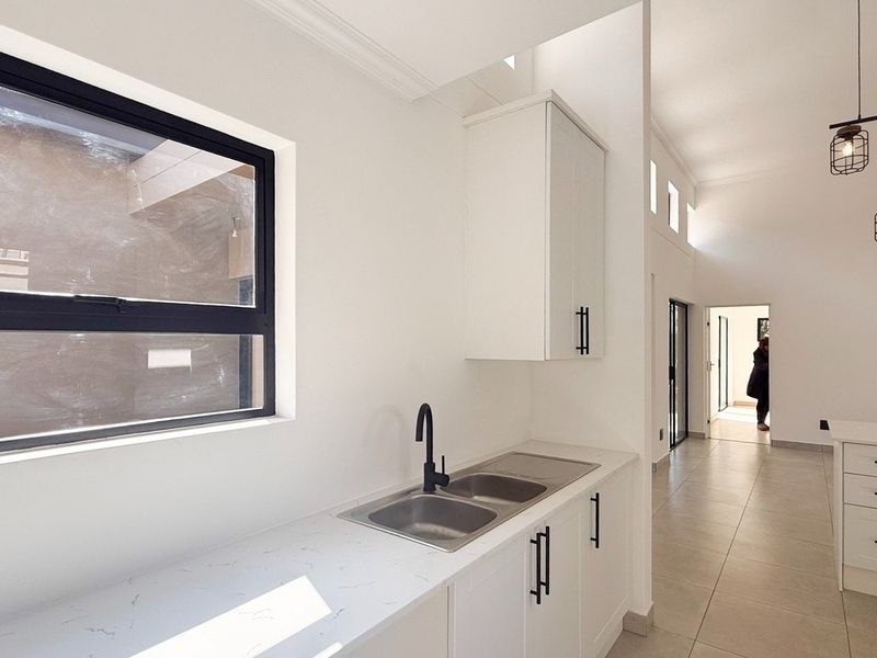 Modern kitchen featuring white cabinetry, stone countertops, double bowl sink, built-in oven, and gas hob, complemented by stylish pendant lighting and tiled flooring.