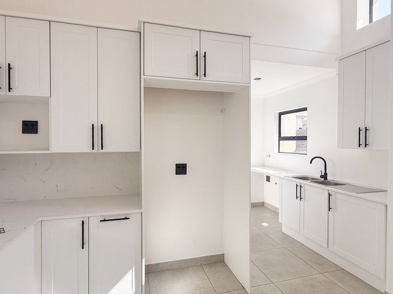 Modern, bright kitchen featuring white shaker cabinetry, stone countertops, a double basin sink with black fixtures, and tiled flooring.