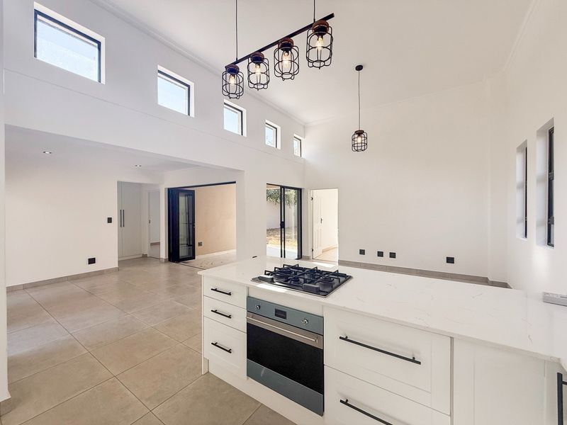 Spacious open-plan living area featuring a modern kitchen island with gas hob, built-in oven, stone countertops, and abundant natural light from clerestory windows.