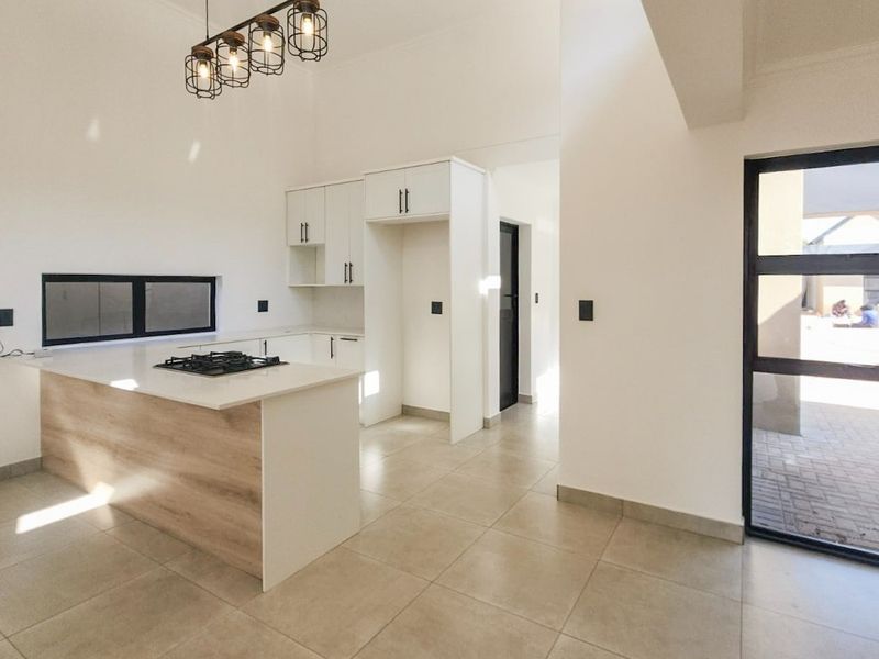 Modern kitchen featuring sleek white cabinetry, a stone-topped island with a built-in gas hob, pendant lighting, and large format floor tiles.