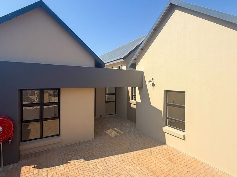A modern townhouse exterior featuring a paved entrance area, clean rendered walls, and contemporary aluminium window frames.