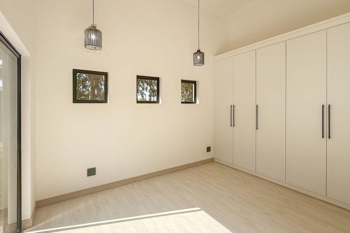 A bright, modern bedroom featuring light laminate flooring, built-in floor-to-ceiling cupboards, and a sliding glass door providing natural light and garden access.