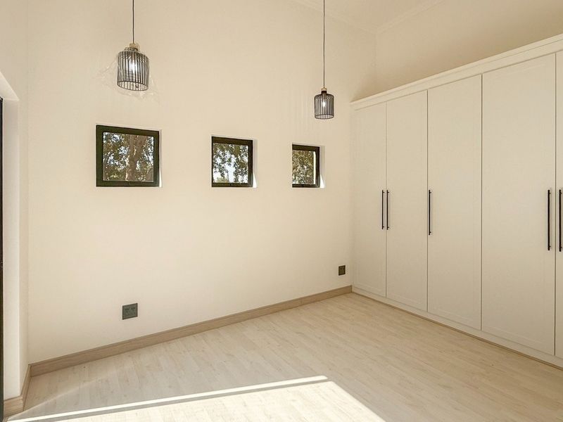 A bright, modern bedroom featuring light laminate flooring, built-in floor-to-ceiling cupboards, and a sliding glass door providing natural light and garden access.