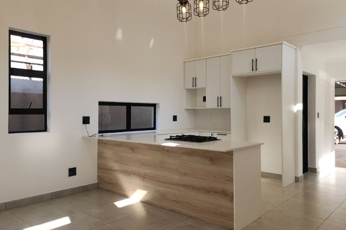 Modern kitchen featuring white cabinetry, wood-look breakfast bar, stone countertops, and a built-in gas hob, set in a bright, open-plan space.