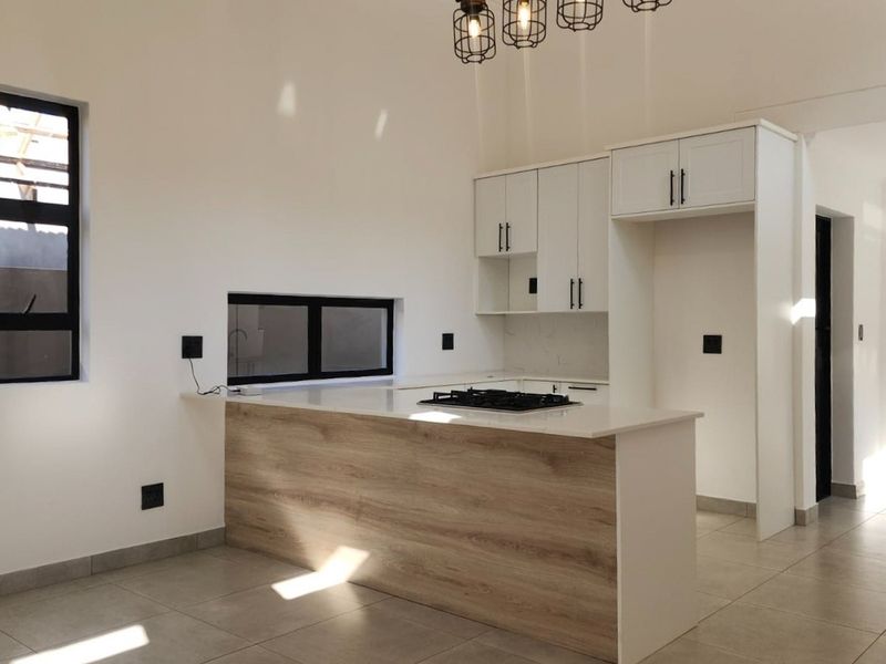 Modern kitchen featuring white cabinetry, wood-look breakfast bar, stone countertops, and a built-in gas hob, set in a bright, open-plan space.