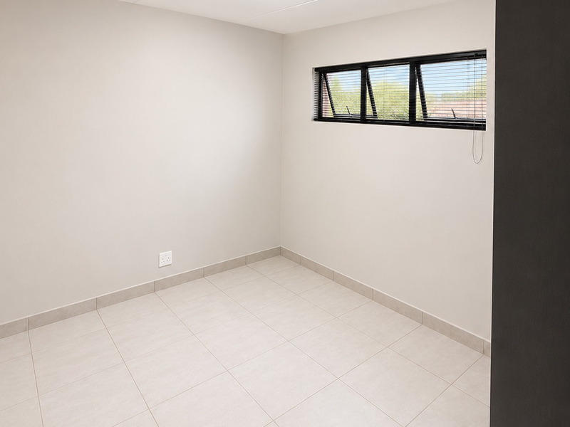 A clean, empty bedroom featuring neutral tiled flooring, smooth walls, and a horizontal window with fitted blinds.