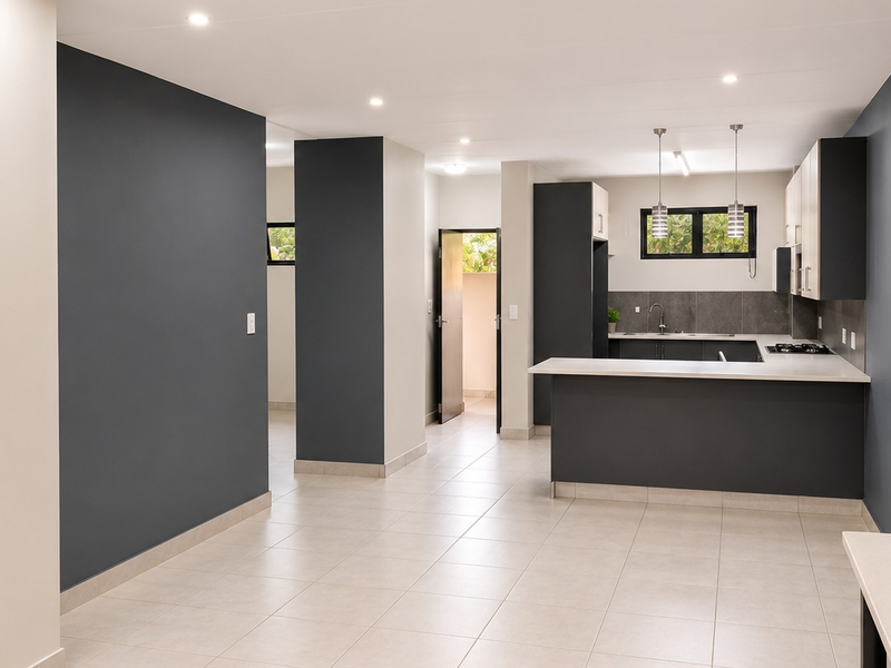 Modern open-plan kitchen and living area featuring sleek cabinetry, stone countertops, built-in hob, and neutral tiled flooring in a well-maintained space.
