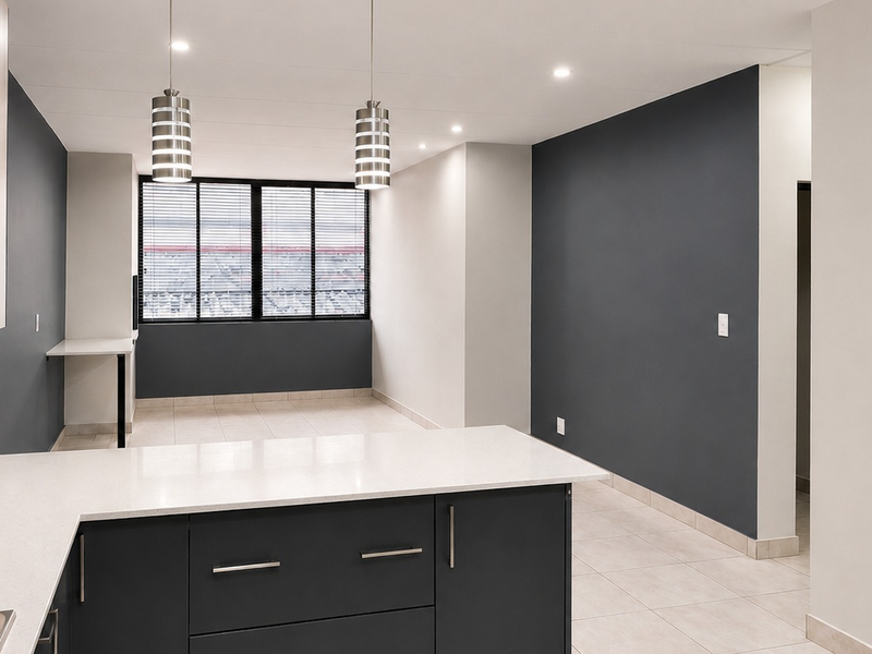 Modern open-plan kitchen and living area featuring sleek cabinetry, stone countertops, integrated hob, and contemporary pendant lighting in a neutral, well-maintained space.
