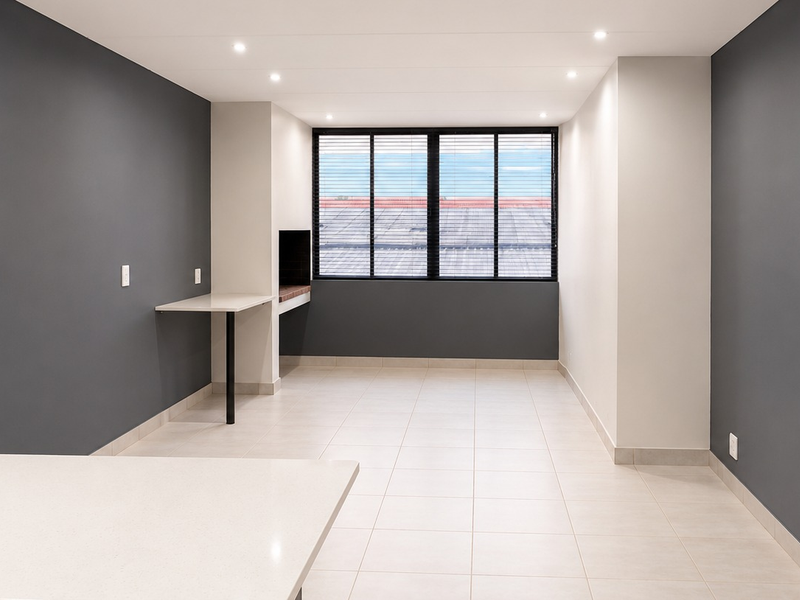 A modern, empty open-plan living area featuring neutral tiled floors, dark accent walls, recessed lighting, and a built-in braai area.