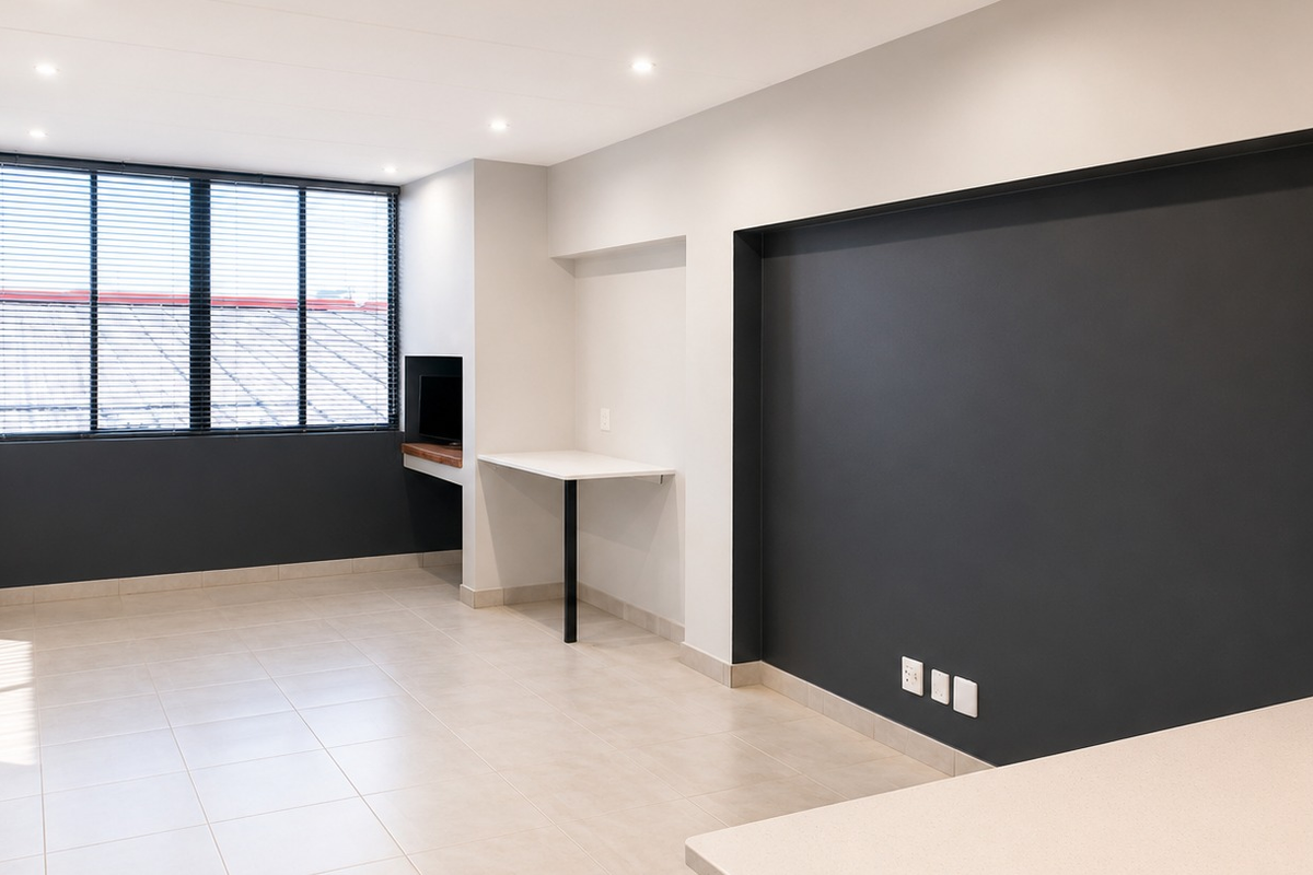 A bright, modern open-plan living area featuring neutral tiled flooring, recessed lighting, and a convenient built-in desk space against a dark accent wall.