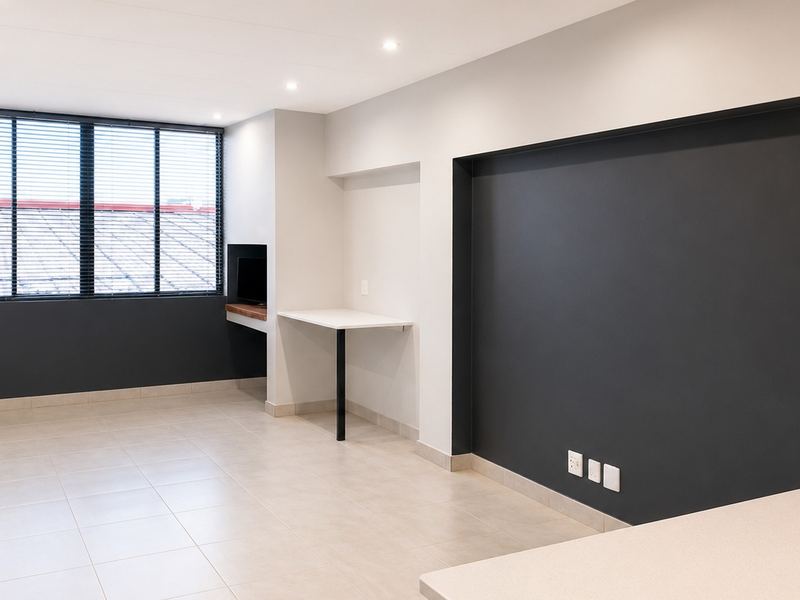 A bright, modern open-plan living area featuring neutral tiled flooring, recessed lighting, and a convenient built-in desk space against a dark accent wall.